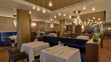 A restaurant with multiple tables set for dining, hanging pendant lights, and a modern interior design.