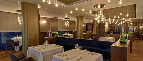 A restaurant with multiple tables set for dining, hanging pendant lights, and a modern interior design.