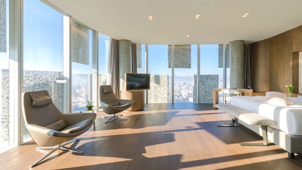 A modern living room with a large TV, comfortable seating, and a city view through floor-to-ceiling windows.