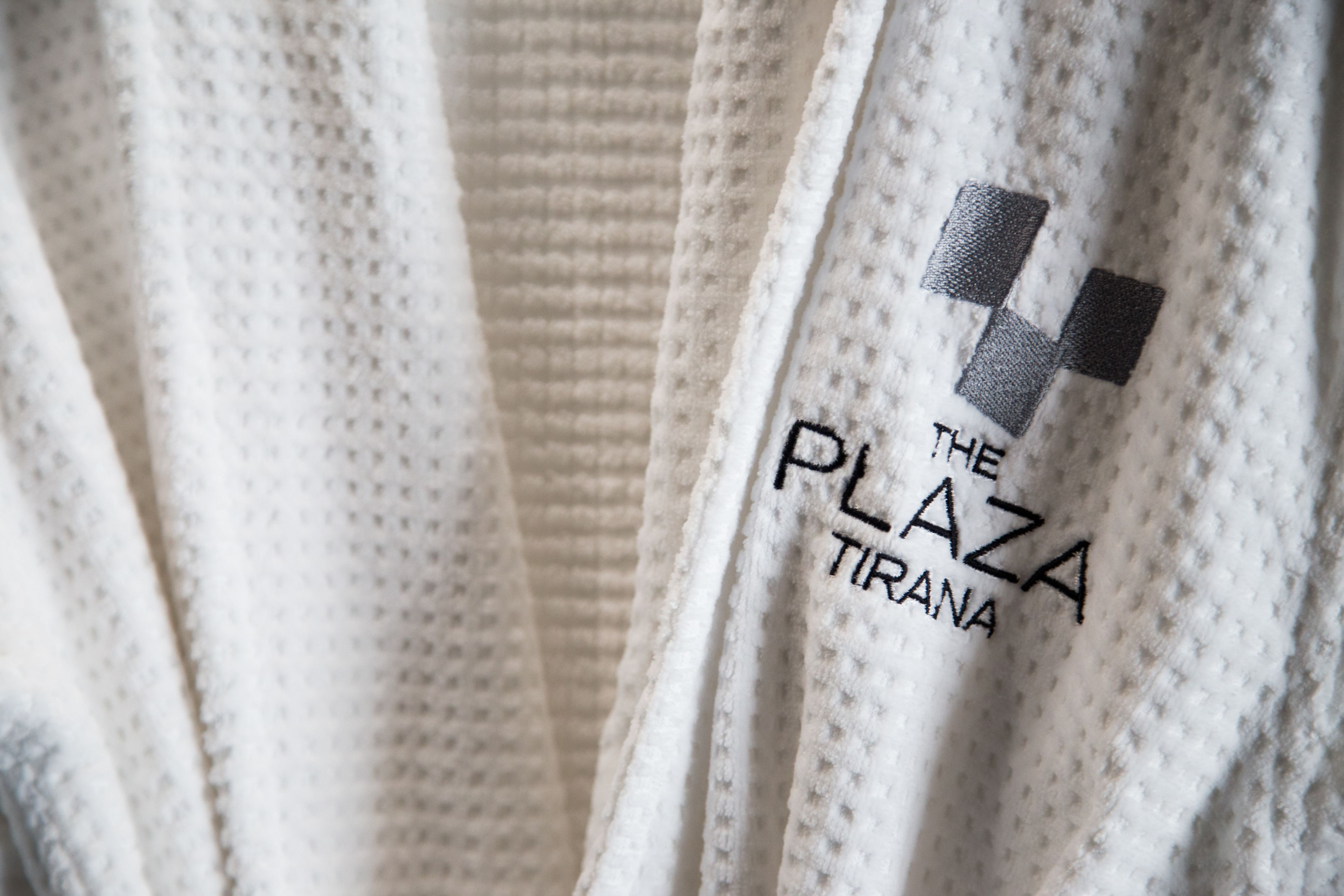 A close-up of a textured fabric with a logo and text reading "THE PLAZA TIRANA".