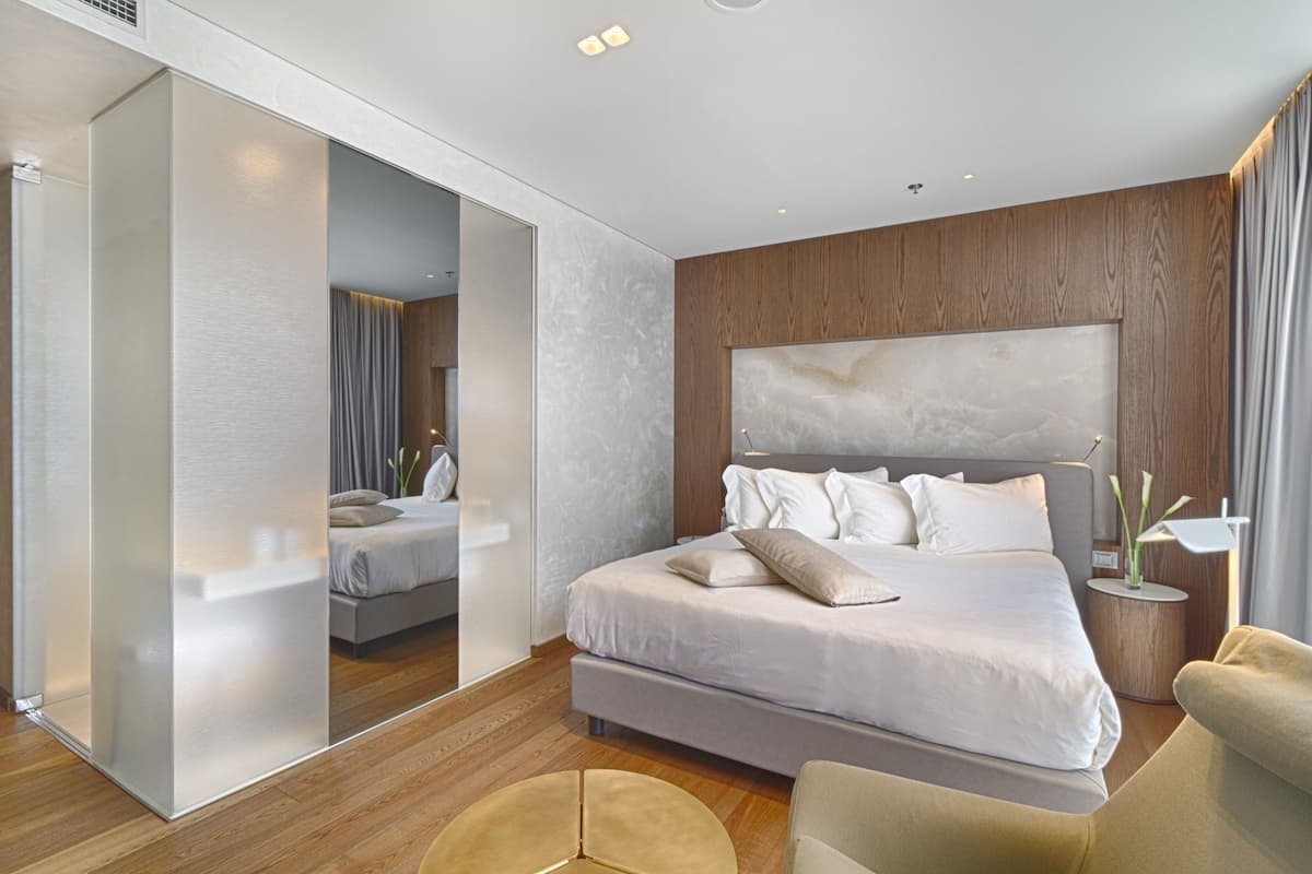 Una habitación de hotel moderna con una cama grande, cabecera de madera, una mesita redonda y un espejo.