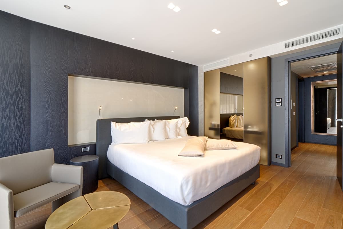 Una habitación de hotel moderna con una cama grande, una zona de estar y un baño visible a través de una puerta abierta.