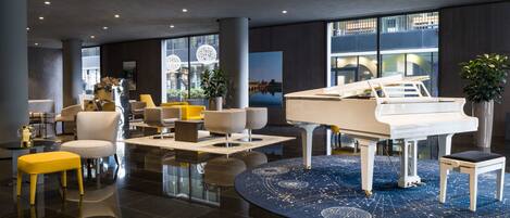 A modern lobby with a grand piano, comfortable seating, and large windows offering views of the city.