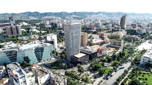 A cityscape with a prominent modern building, a mix of residential and commercial structures, and a mountainous backdrop.