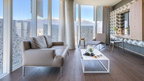A modern living room with a sofa, coffee table, and dining area, featuring large windows with a mountain view.