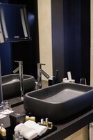 Un baño moderno con un lavamanos negro grande, dos grifos cromados y un espejo arriba.