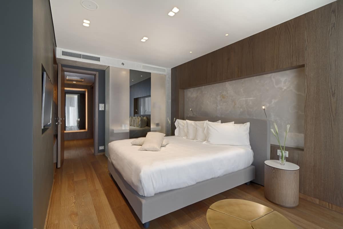 Un dormitorio moderno con una cama grande, cabecera de madera y una mesita de noche con un florero.