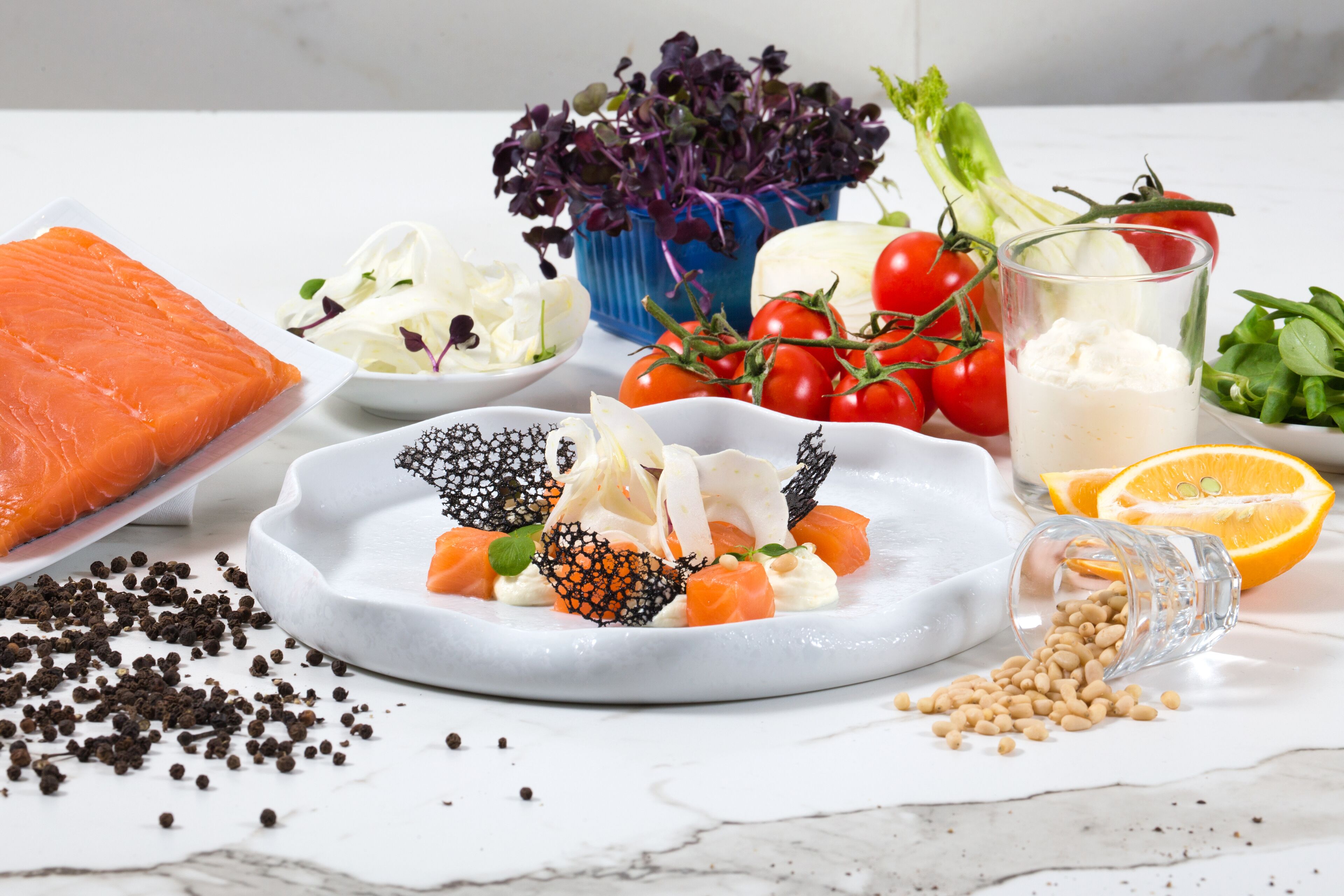 Une variété d’ingrédients frais, notamment du saumon, des tomates et des légumes verts à feuilles, disposés sur une surface en marbre.
