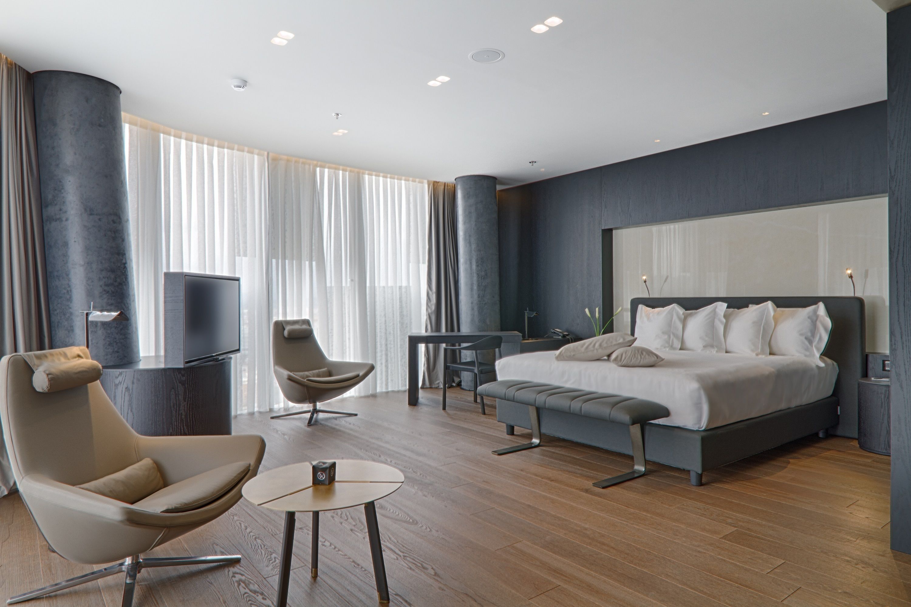 A modern hotel room with a large bed, a desk, a chair, and a television.