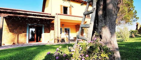 A rustic building with a stone facade, a wooden pergola, and a well-maintained garden with purple flowers.