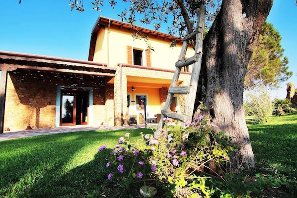 A rustic building with a stone facade, a wooden pergola, and a well-maintained garden with purple flowers.