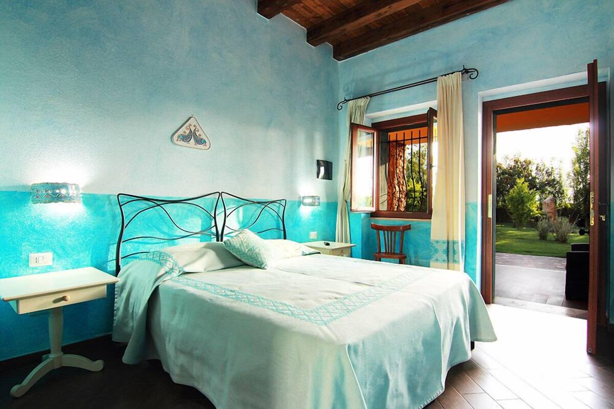 A bedroom with a bed, bedside tables, a window with curtains, and a view of the outdoors.