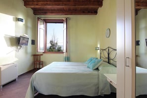 A bedroom with a bed, a chair, a television on the wall, and a window with a view of trees.