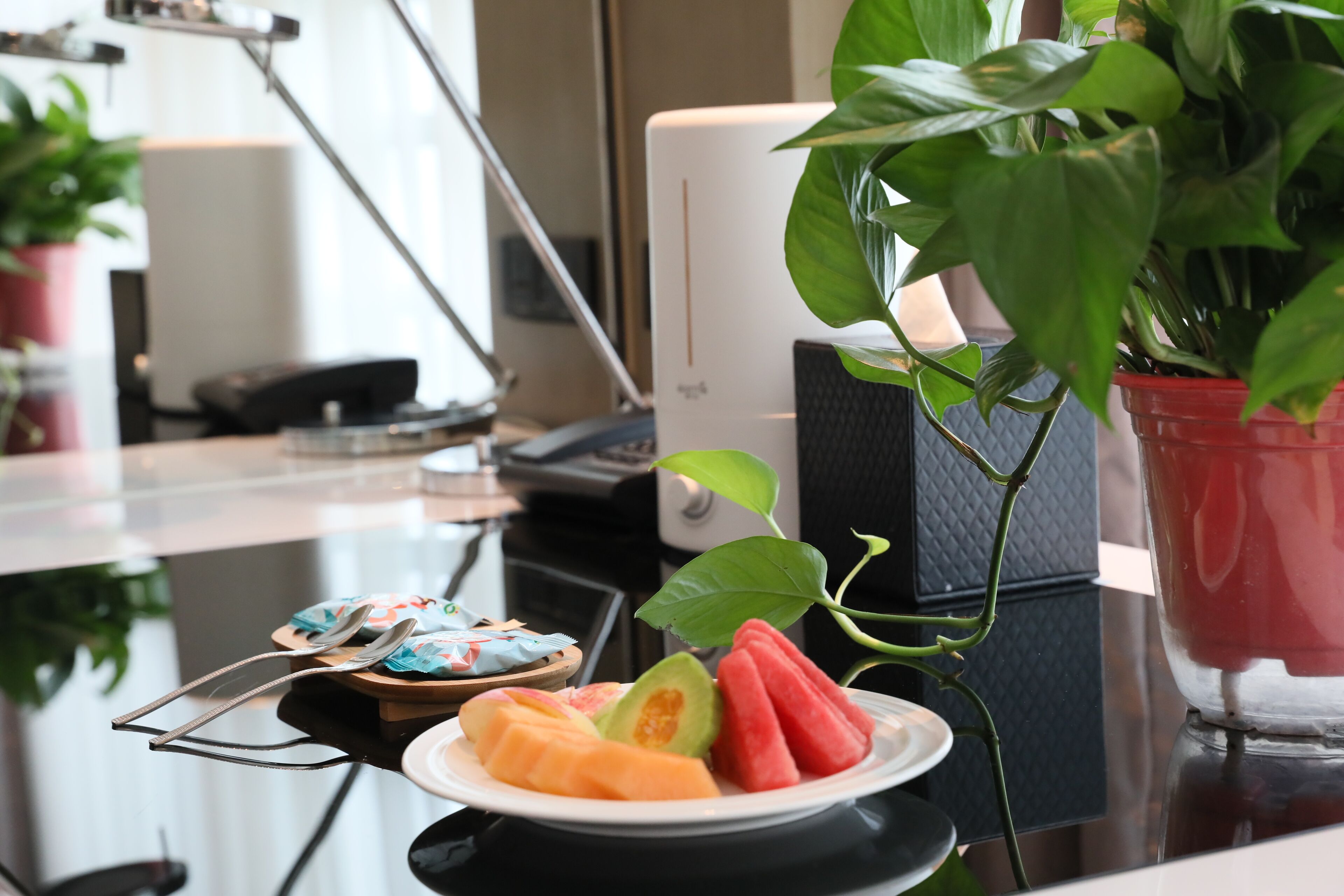 Un escritorio con una bandeja de fruta, una planta en maceta y un monitor de computadora.