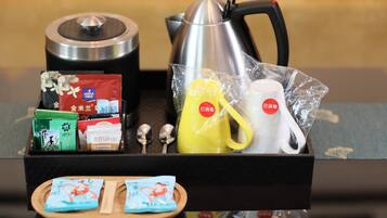 A tray with tea bags, a teapot, a yellow mug, and a white mug, all in a black tray.