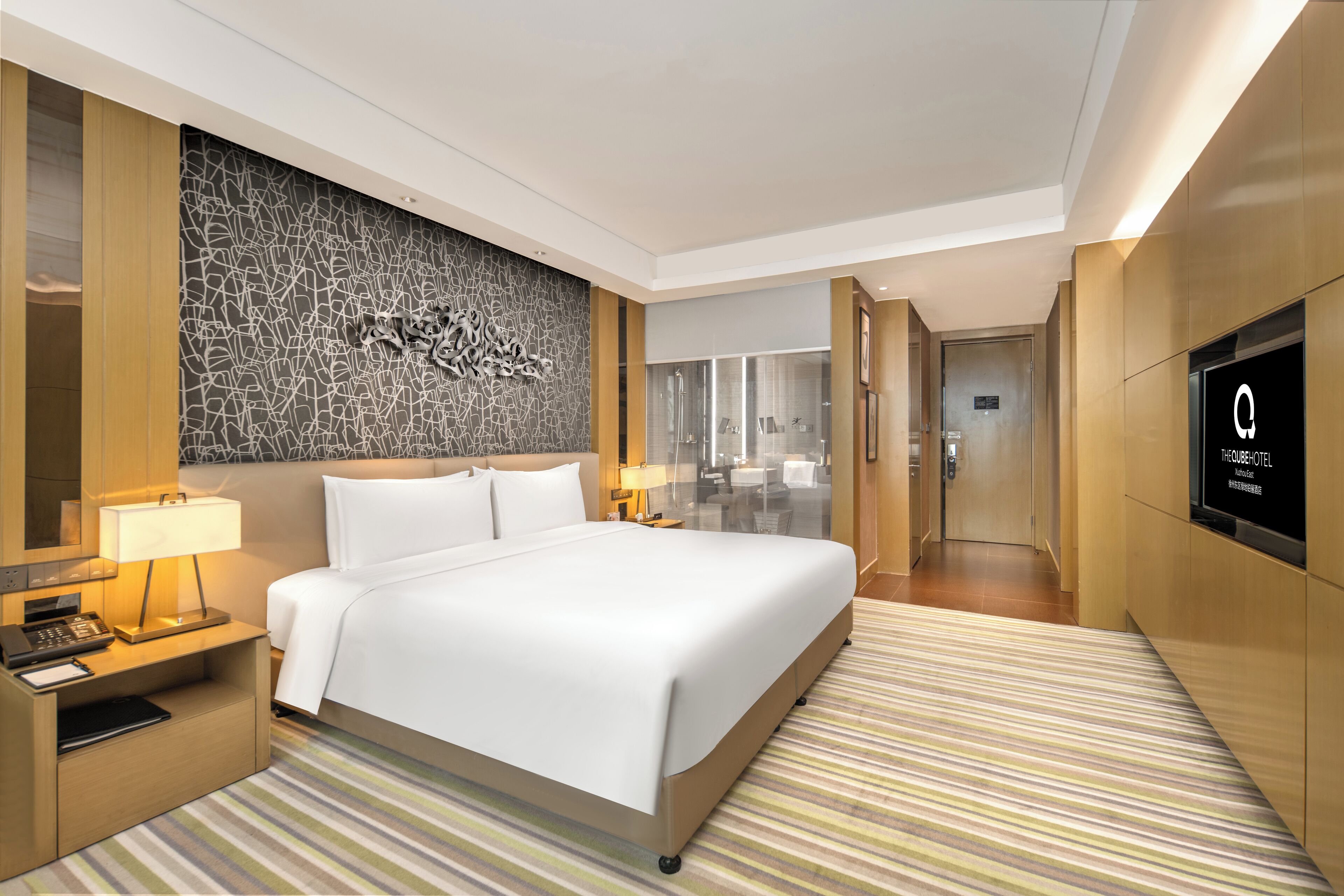 Una habitación de hotel moderna con una cama grande, mesitas de noche con lámparas, un adorno en la pared y un televisor montado en la pared.