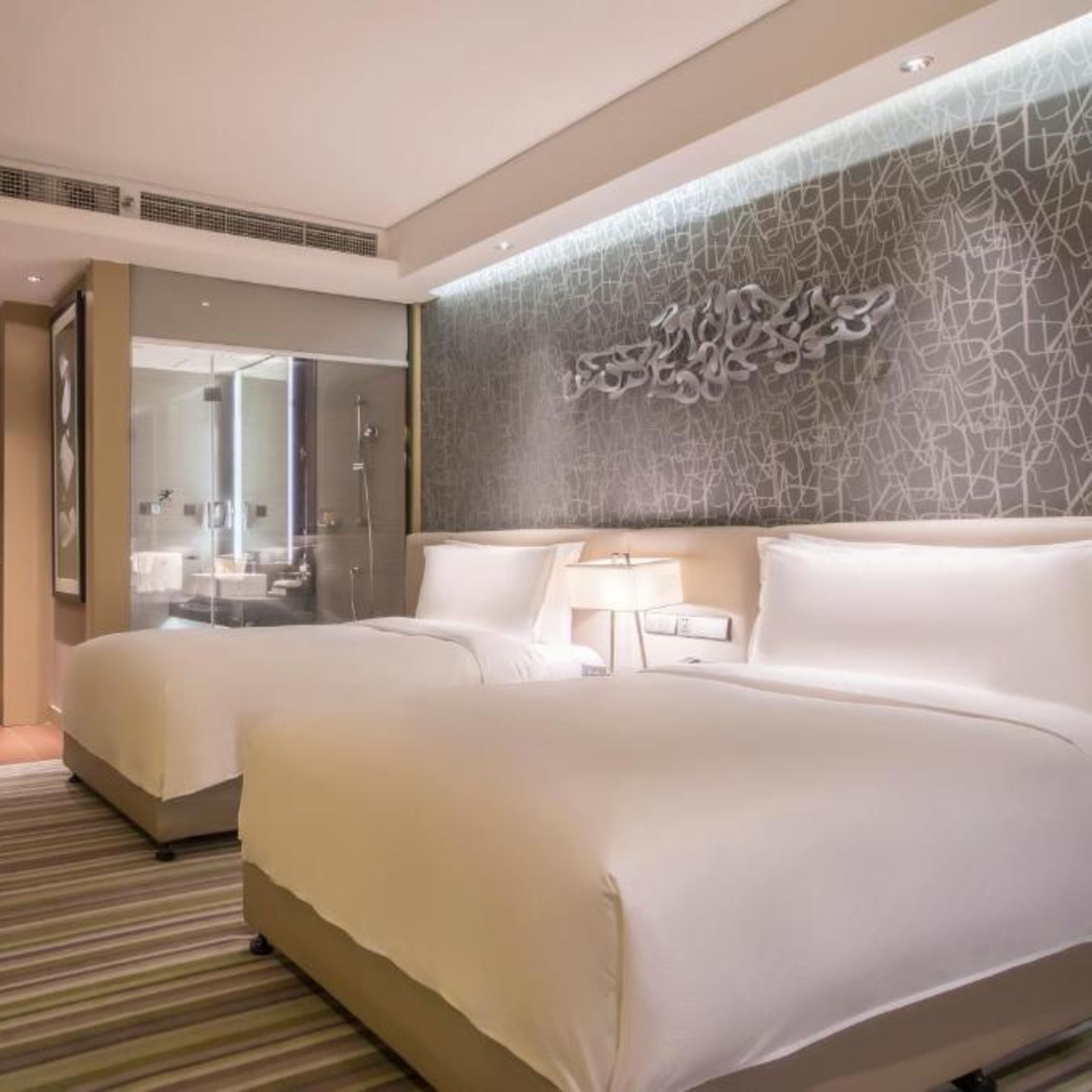 Una habitación de hotel moderna con dos camas, un espejo grande y un diseño de pared con textura.