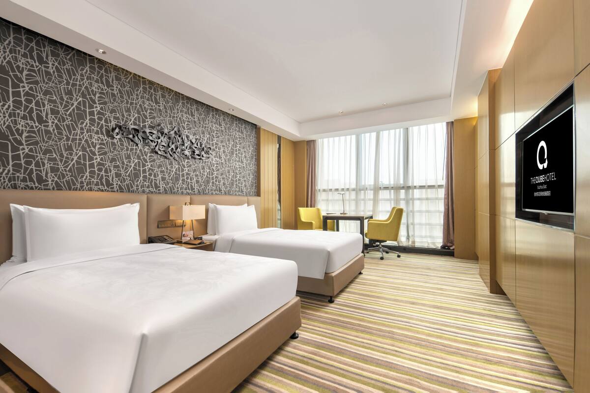 Une chambre d’hôtel avec deux lits, une télévision, un bureau et une fenêtre avec des rideaux.