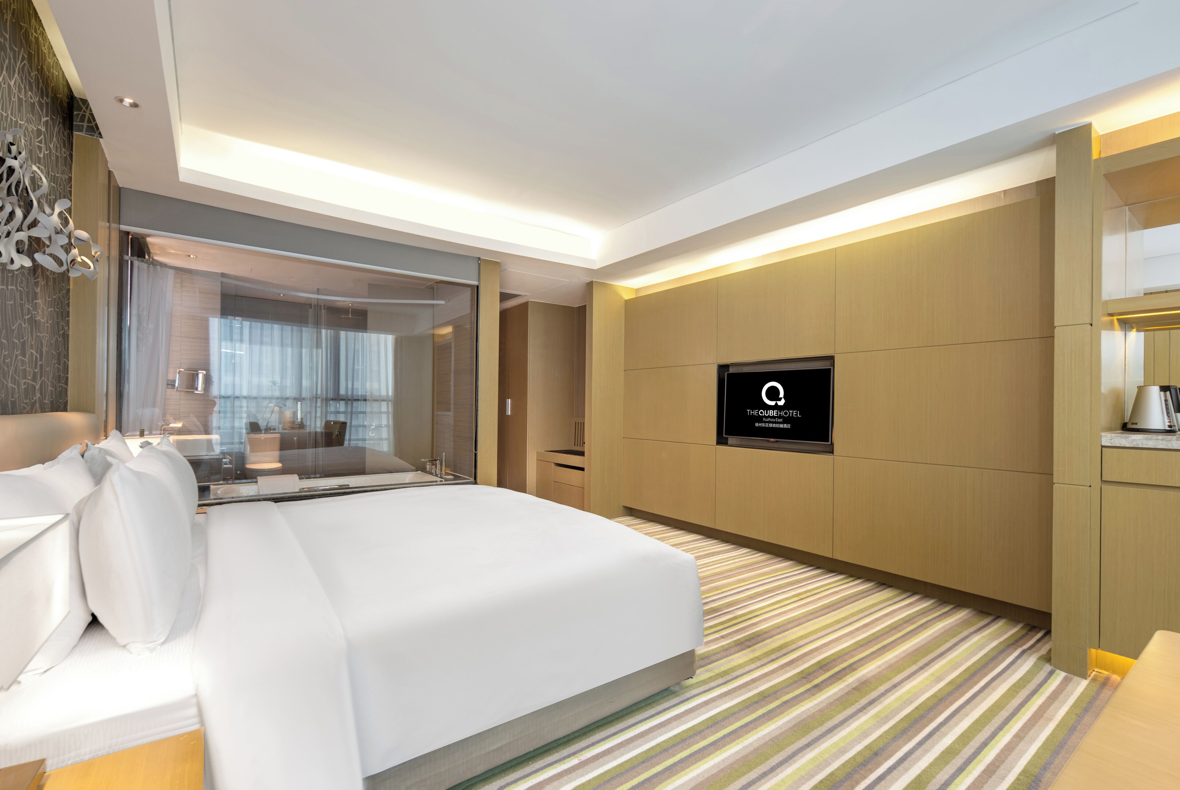A modern hotel room with a large bed, a TV, and a view of the city through the window.