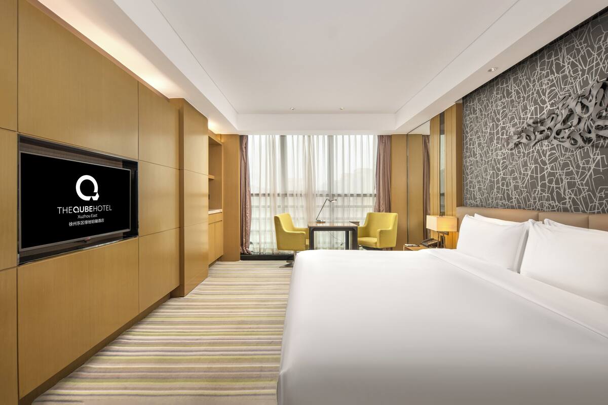 Une chambre d’hôtel avec un grand lit, un téléviseur fixé au mur, un bureau avec deux chaises et une fenêtre avec des rideaux.