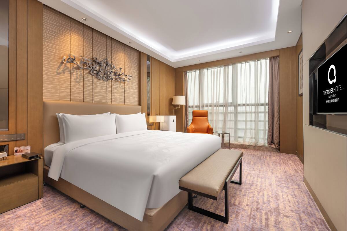 Une chambre d’hôtel avec un grand lit, un banc, une télévision et une fenêtre avec des rideaux.