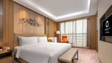 Una habitación de hotel con una cama grande, un banco, un televisor y una ventana con cortinas.