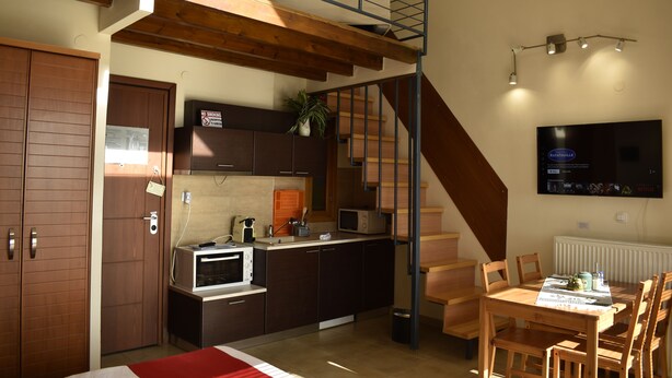 Een kleine keuken met een eethoek, een trap en een aan de muur bevestigde televisie.