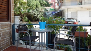 Een balkon met twee stoelen en een kleine tafel, omringd door potplanten en uitzicht op een straat met gebouwen en geparkeerde auto's.