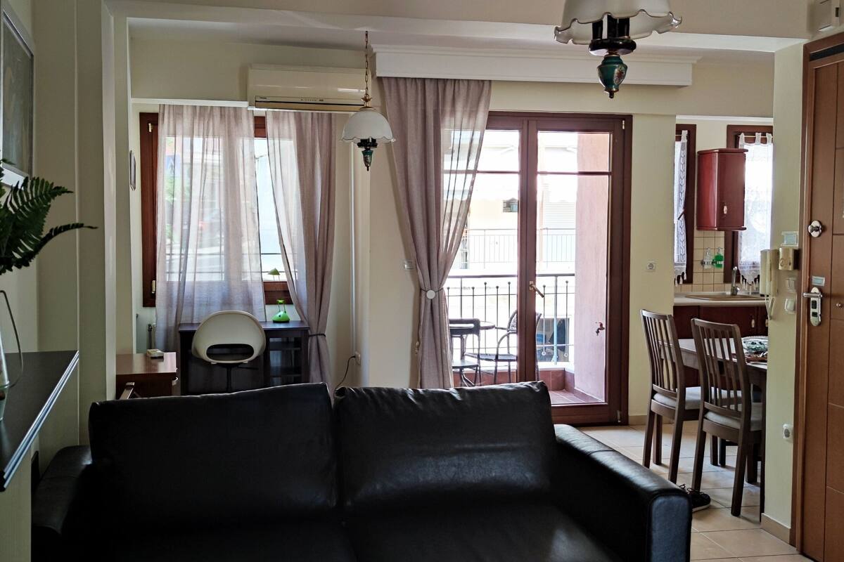 Ein Wohnzimmer mit grauem Sofa, einem Essbereich mit Tisch und Stühlen sowie einer Küchenzeile mit Schränken und Arbeitsplatte.