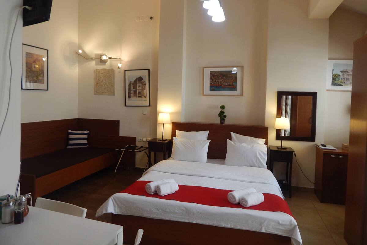 Ein Hotelzimmer mit einem großen Bett, einem Holzkopfbrett, einer roten Tagesdecke und zwei Nachttischlampen.
