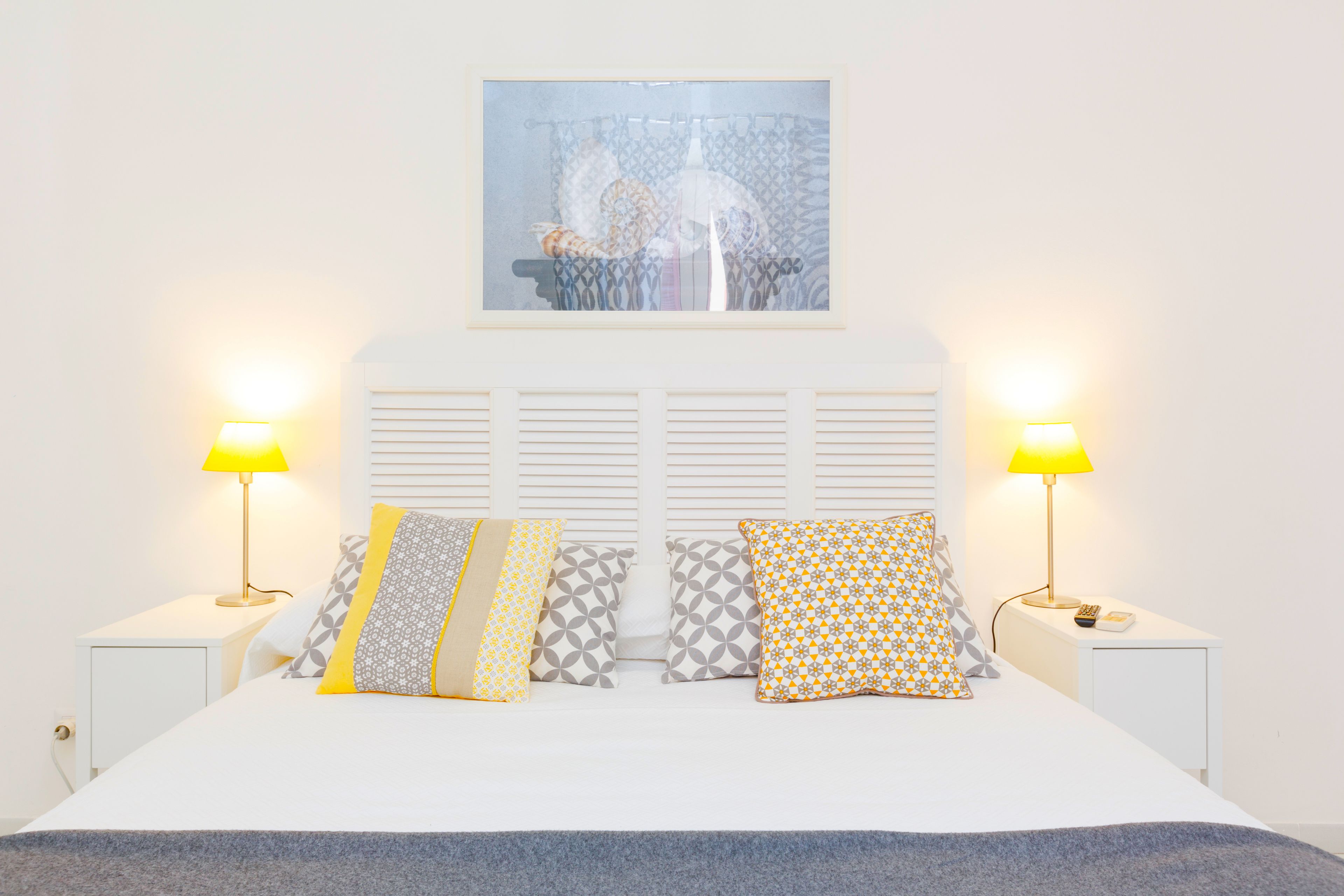 A neatly arranged bedroom with a bed, two bedside lamps, and a framed artwork above the headboard.