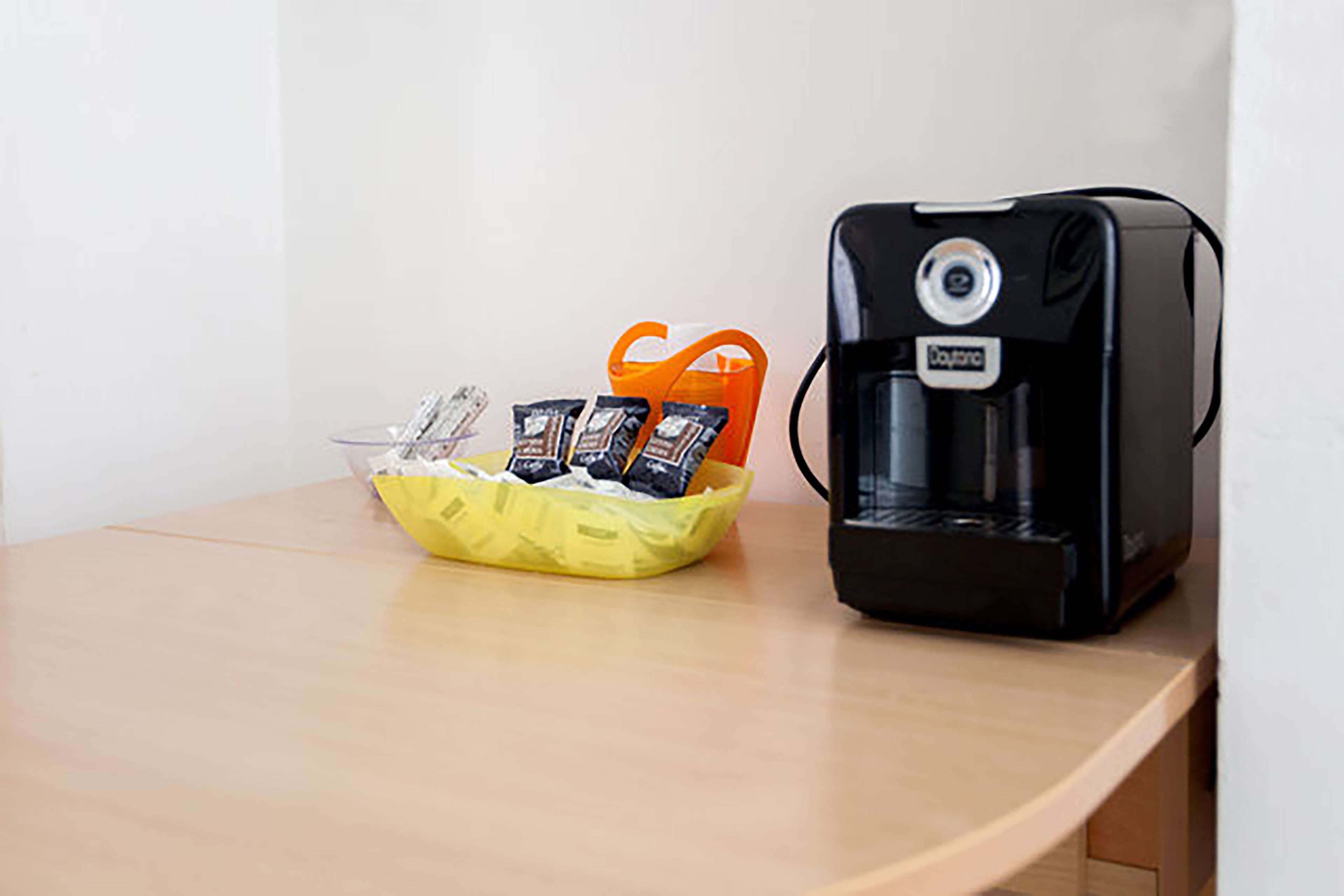 A coffee maker and a basket with packets on a wooden table.