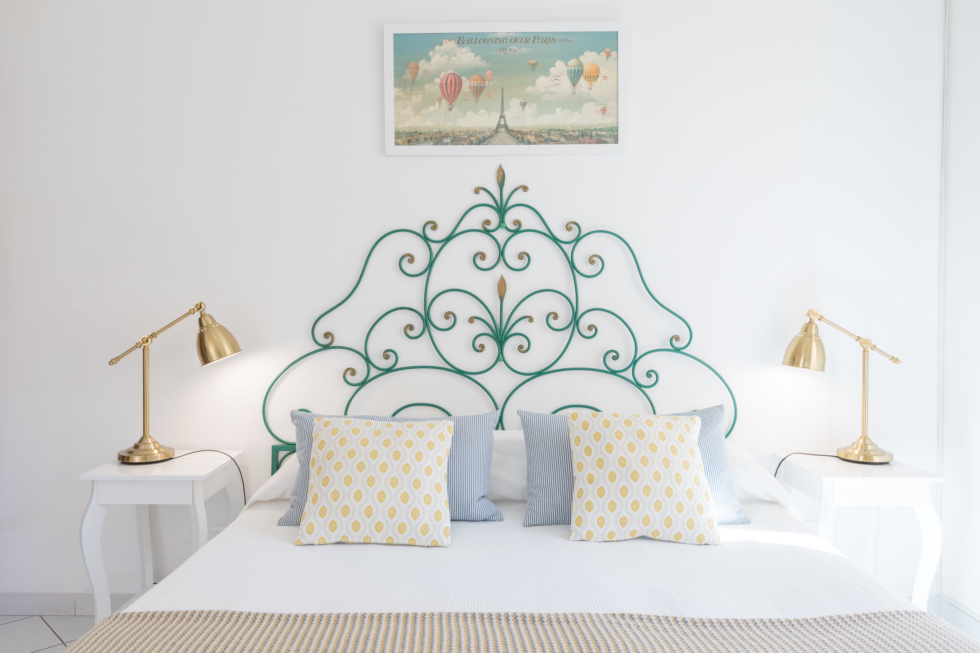 Een net opgemaakt bed met gestreepte kussens, een decoratief hoofdbord en twee bedlampen.