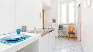 A modern kitchen with white cabinets, a stainless steel sink, and a compact dining area with a blue tablecloth. - B&B Piazza Fratti (Civitavecchia)