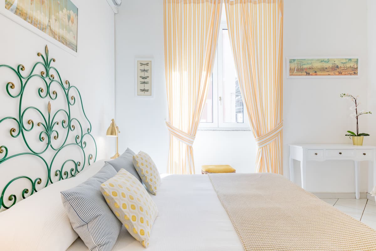 A bedroom with a bed, curtains, a desk, and a wall with artwork.