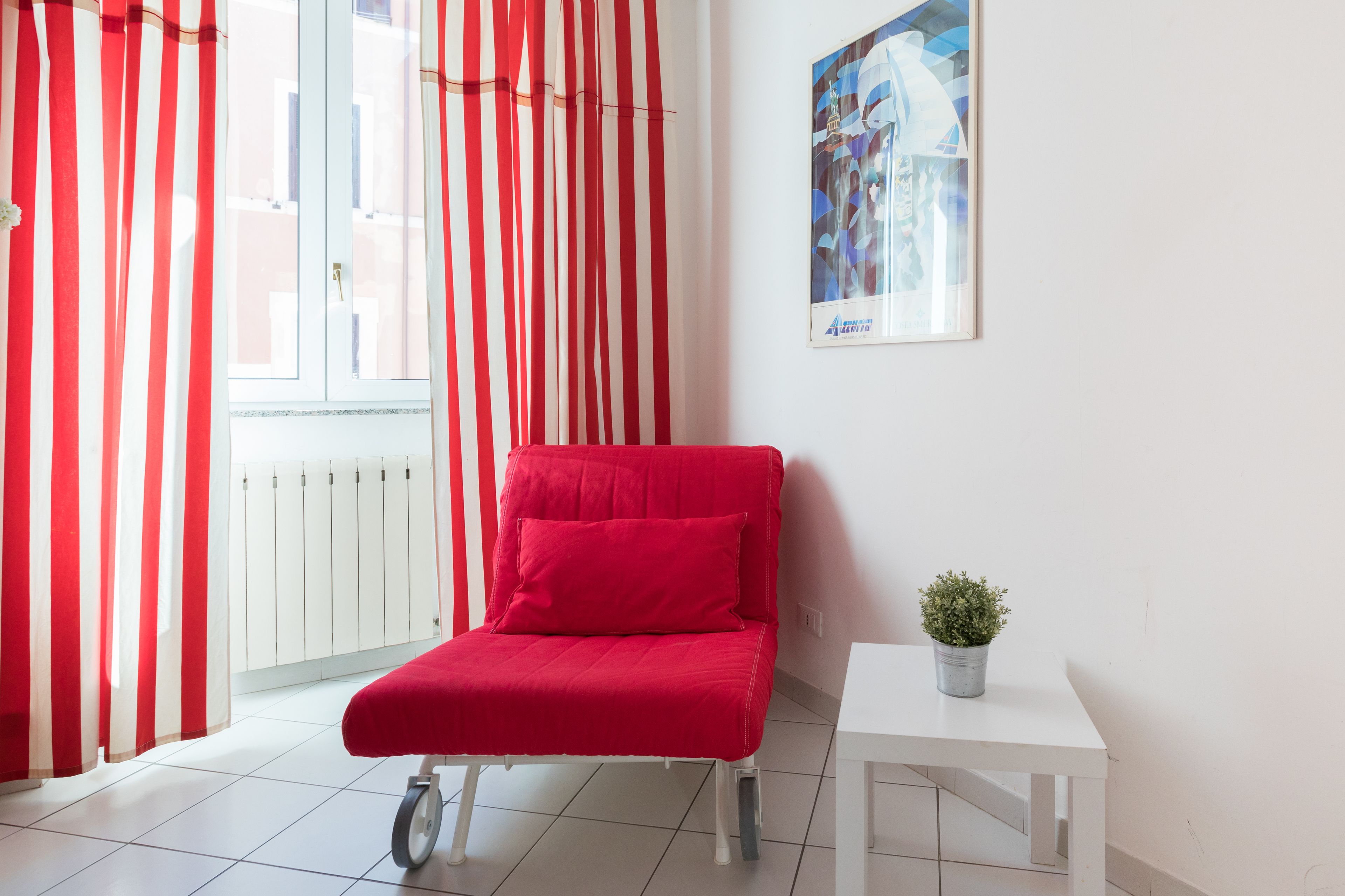 Une pièce avec une chaise rouge, une petite table sur laquelle se trouve une plante, et une fenêtre ornée de rideaux rouges et blancs.