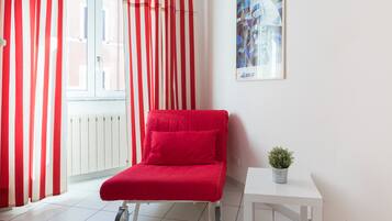 Une pièce avec une chaise rouge, une petite table sur laquelle se trouve une plante, et une fenêtre ornée de rideaux rouges et blancs.