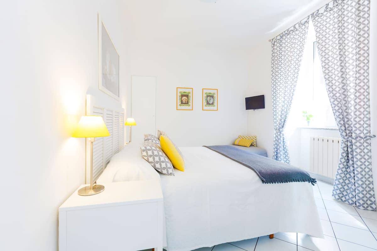 A bedroom with a bed, bedside lamps, a TV, and patterned curtains.