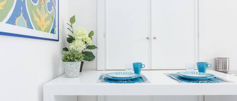 Un área de comedor blanca con una mesa dispuesta para dos, con platos y una taza azules.