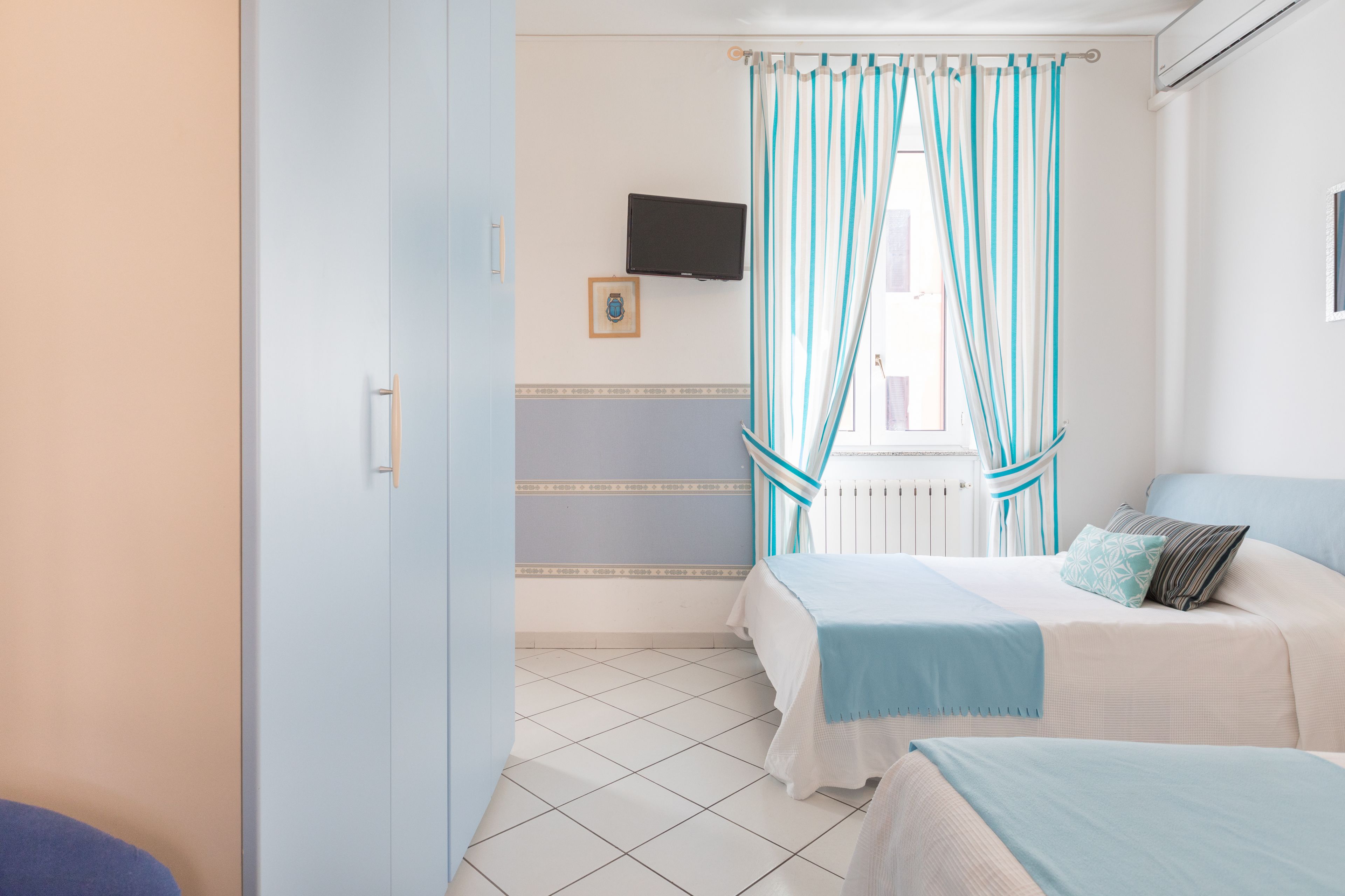 Un dormitorio con dos camas, un televisor en la pared y una ventana con cortinas a rayas.