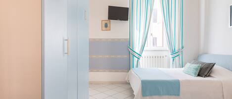 Un dormitorio con dos camas, un televisor en la pared y una ventana con cortinas a rayas.