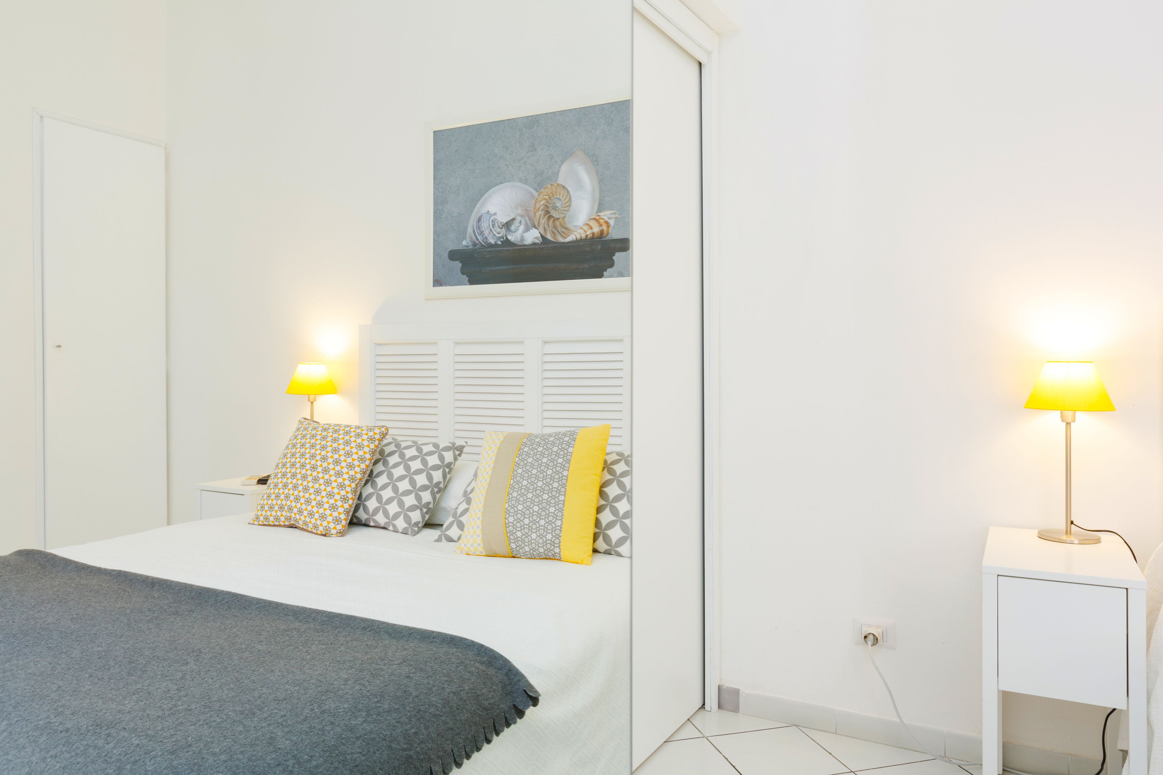 Une chambre à coucher bien rangée, avec un lit, des tables de chevet et une œuvre d’art accrochée au mur.