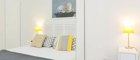 Une chambre à coucher bien rangée, avec un lit, des tables de chevet et une œuvre d’art accrochée au mur.