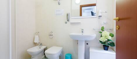 A bathroom with a bidet, toilet, sink, and a mirror.
