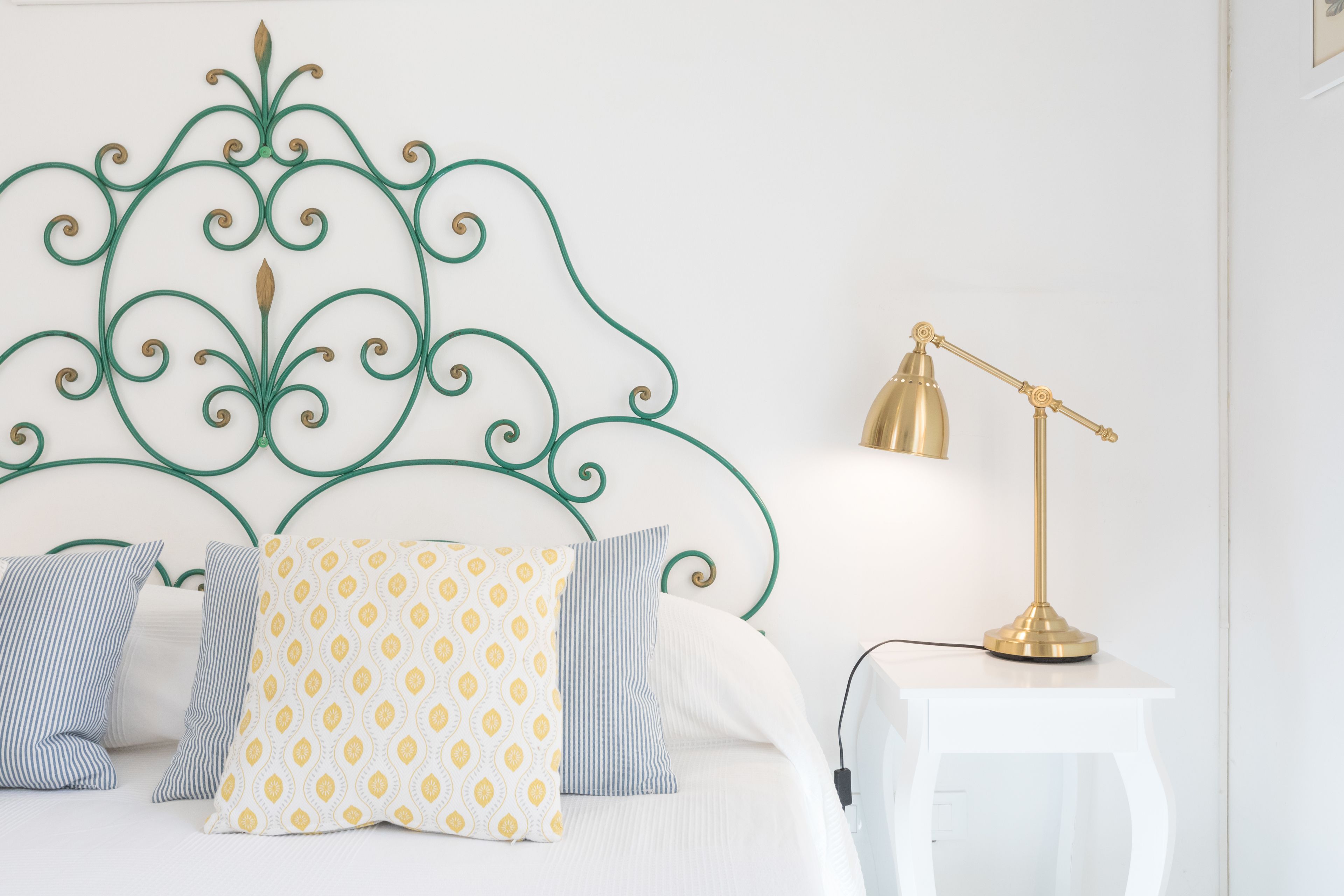 A neatly made bed with patterned pillows, a decorative metal headboard, and a bedside table with a lamp.