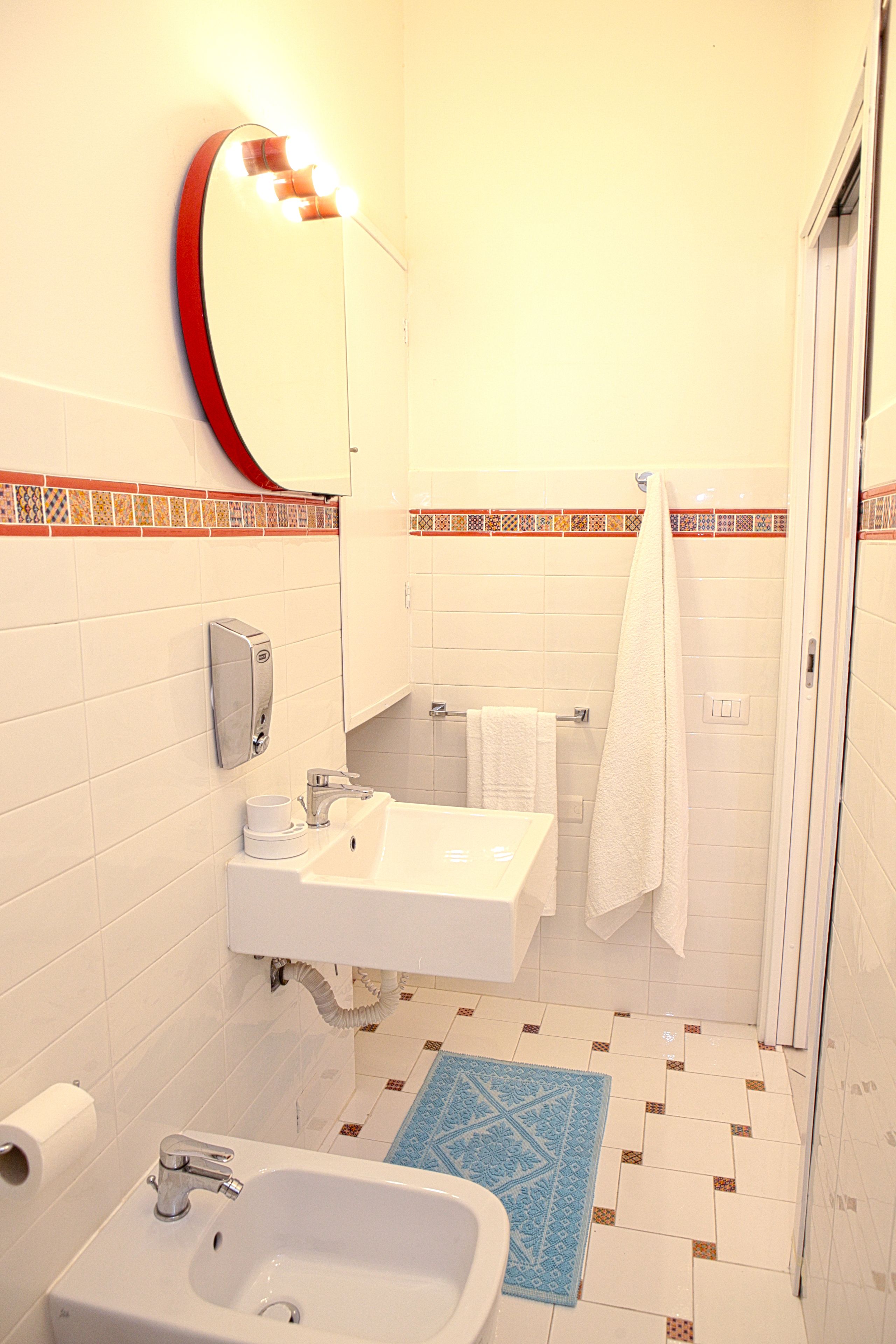 A bathroom with a white sink, mirror, and toilet. There is a blue rug on the floor and a towel hanging on the wall.