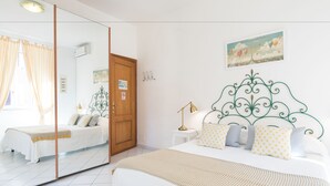 A bedroom with a large mirror, a bed with white bedding, a nightstand, a lamp, and a painting on the wall. - B&B Piazza Fratti (Civitavecchia)