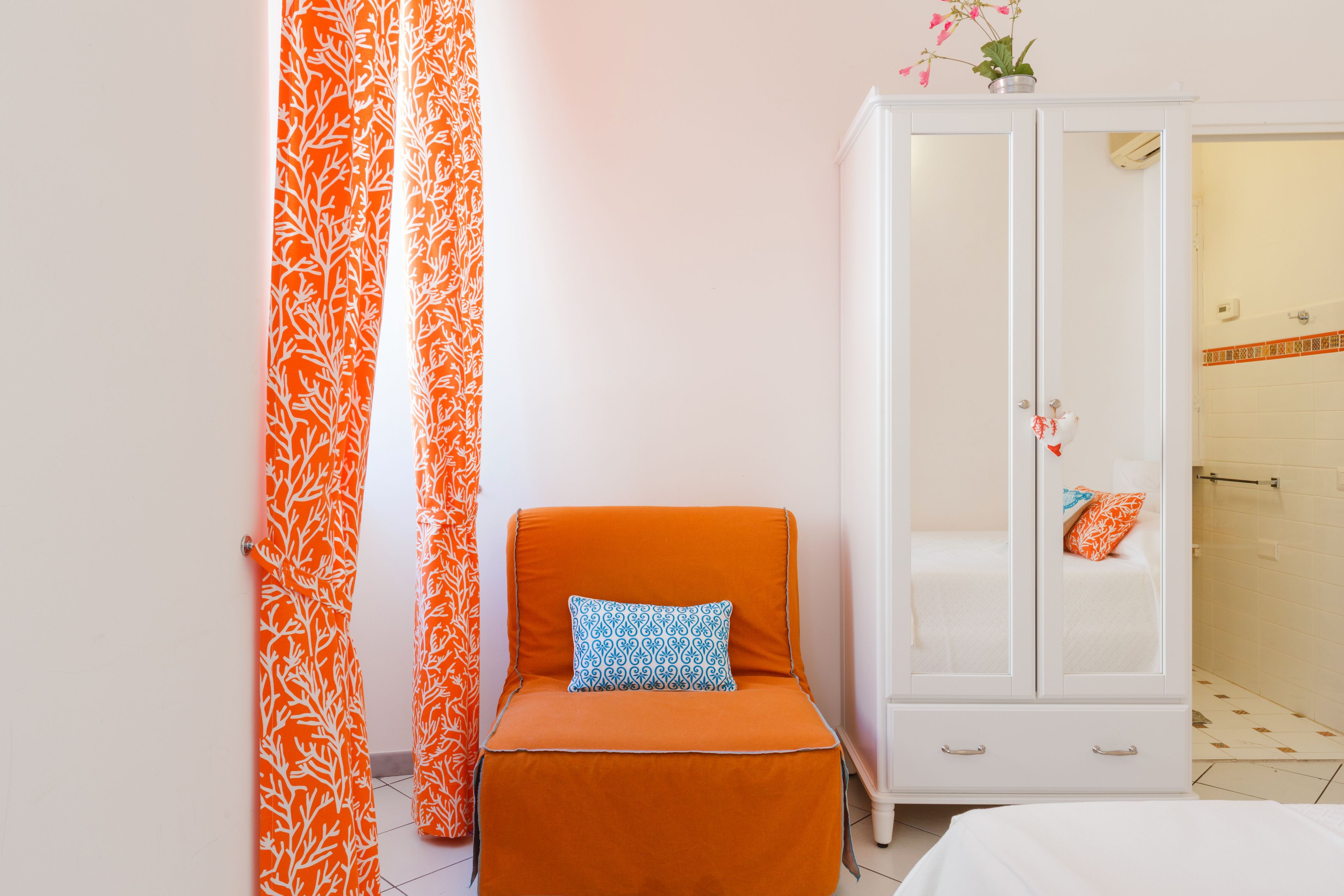 Una habitación con una sola silla naranja, un armario blanco y una cama.