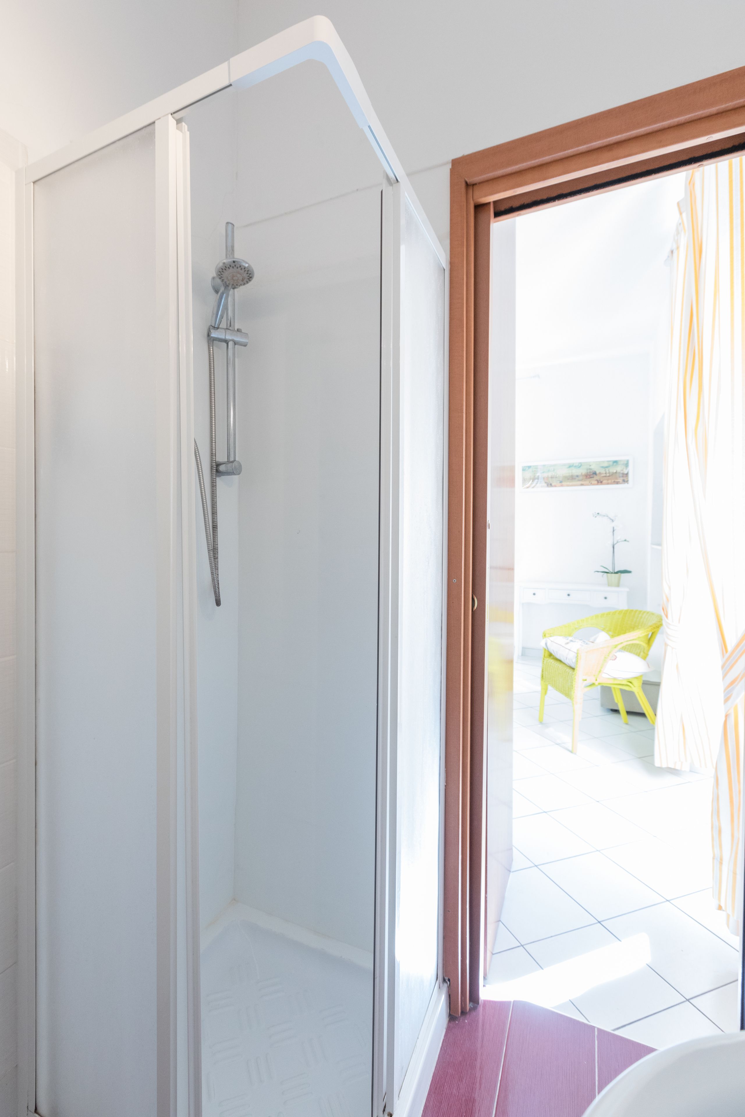 Un baño moderno con cabina de ducha de vidrio, un lavabo blanco y una silla amarilla en la habitación contigua.