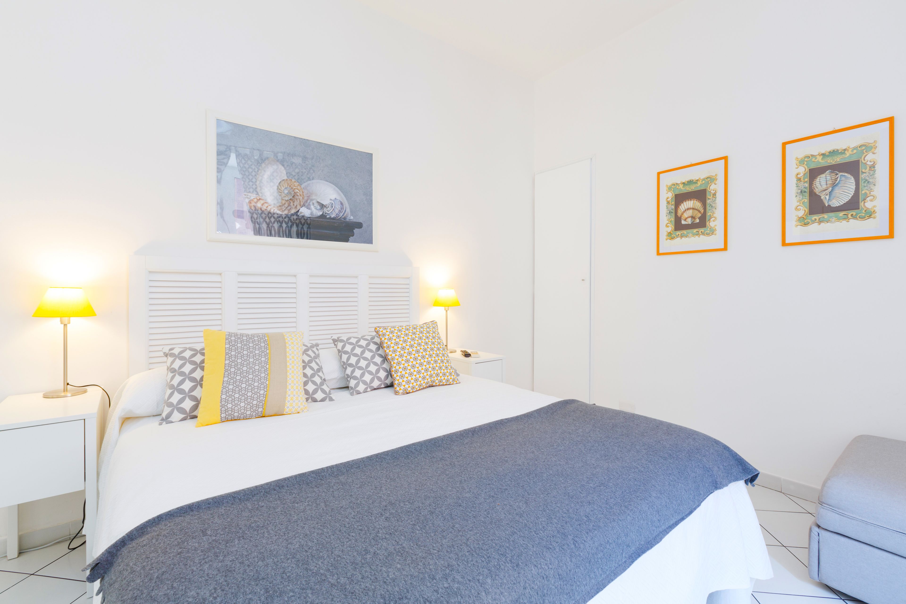 Un dormitorio ordenado con una cama, lámparas de noche y cuadros en la pared.